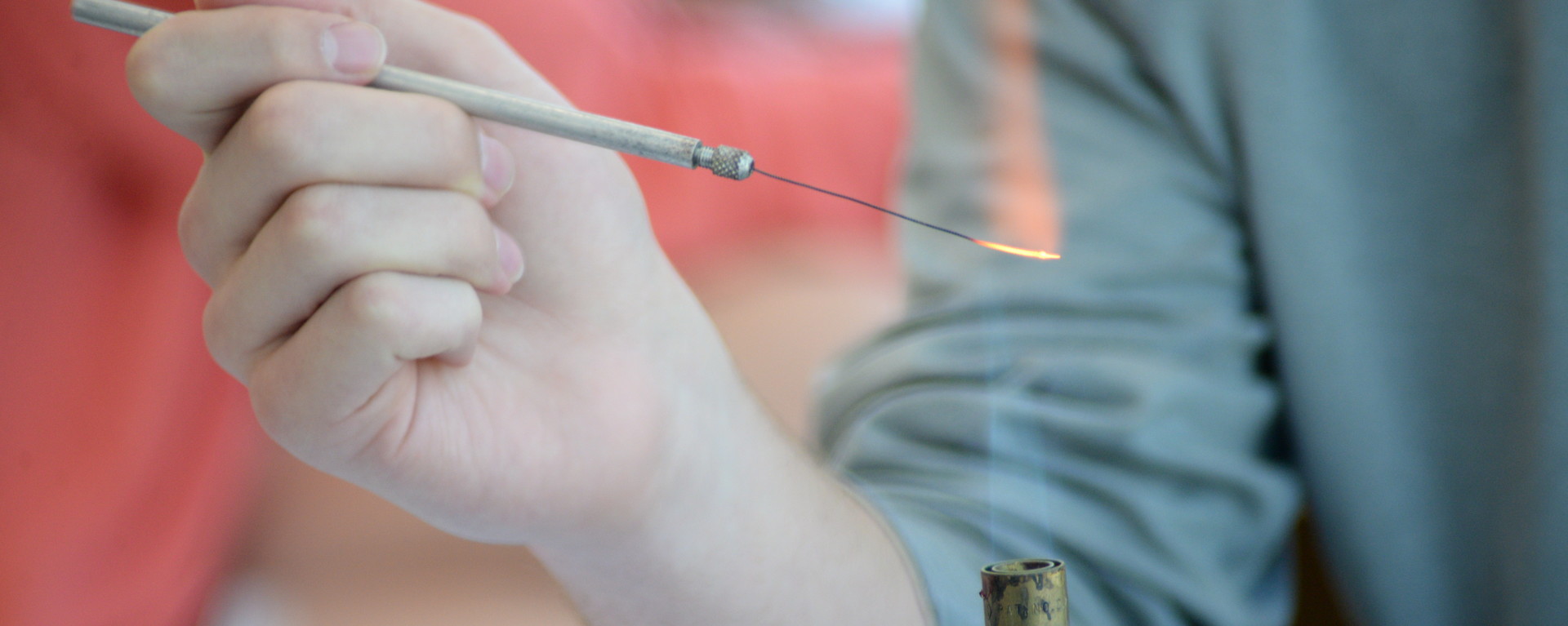 Student's hand holding a lab instrument over flame